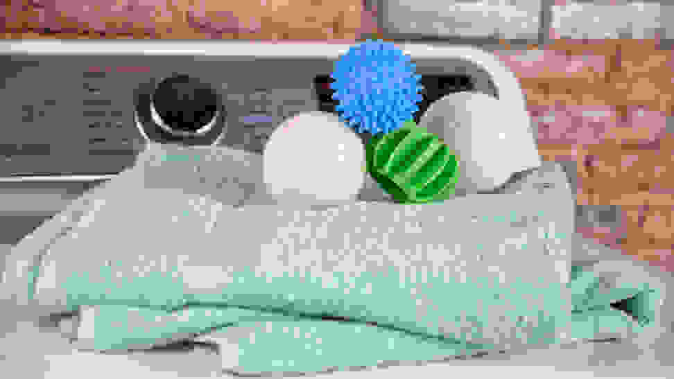 Four different brands of the best dryer balls are photographed atop a couple soft blue towels on the lid of a dryer.