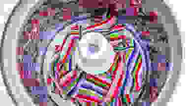 An overhead view of a top-load washer with agitator which is filled with striped sheets.